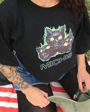 Remera negra crop top con estampa de 3 gatos furiosos y en llamas. Debajo una palabra: michis